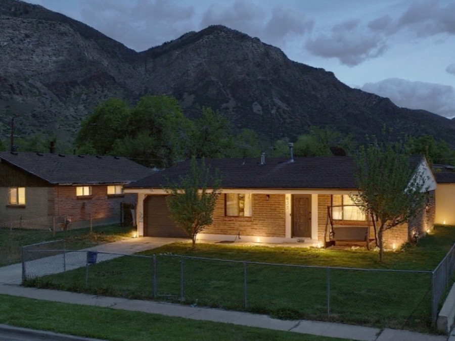 Single-storey brick rambler lit at dusk, with a covered porch swing and a mountain ridge behind it.